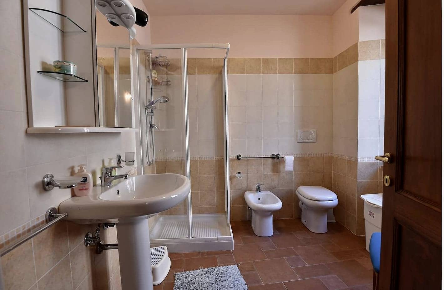 Bagno con doccia, lavabo a colonna, bidè e pavimento in cotto