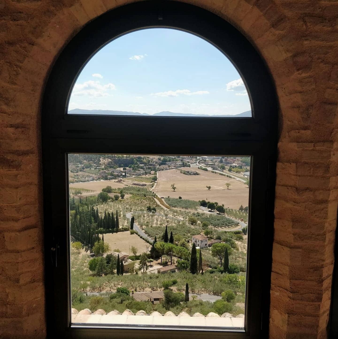 Un finestrone ad arco della loggia che incornicia gli uliveti e i cipressi della valle