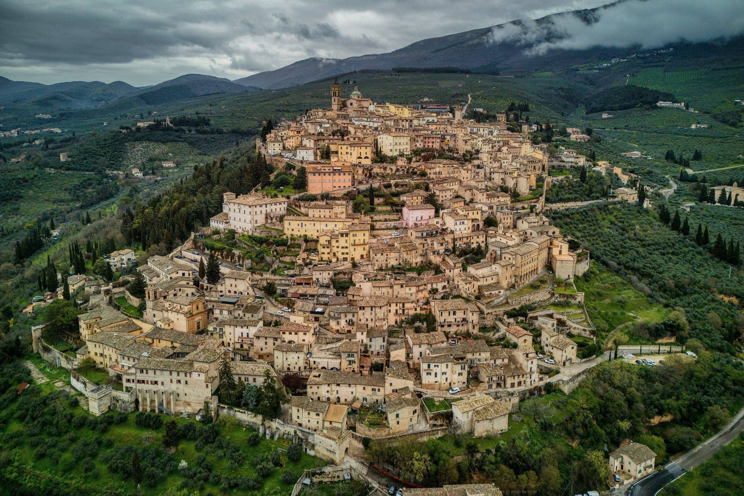 Trevi sul colle vista dall'alto, tra uliveti e boschi, con le montagne sullo sfondo